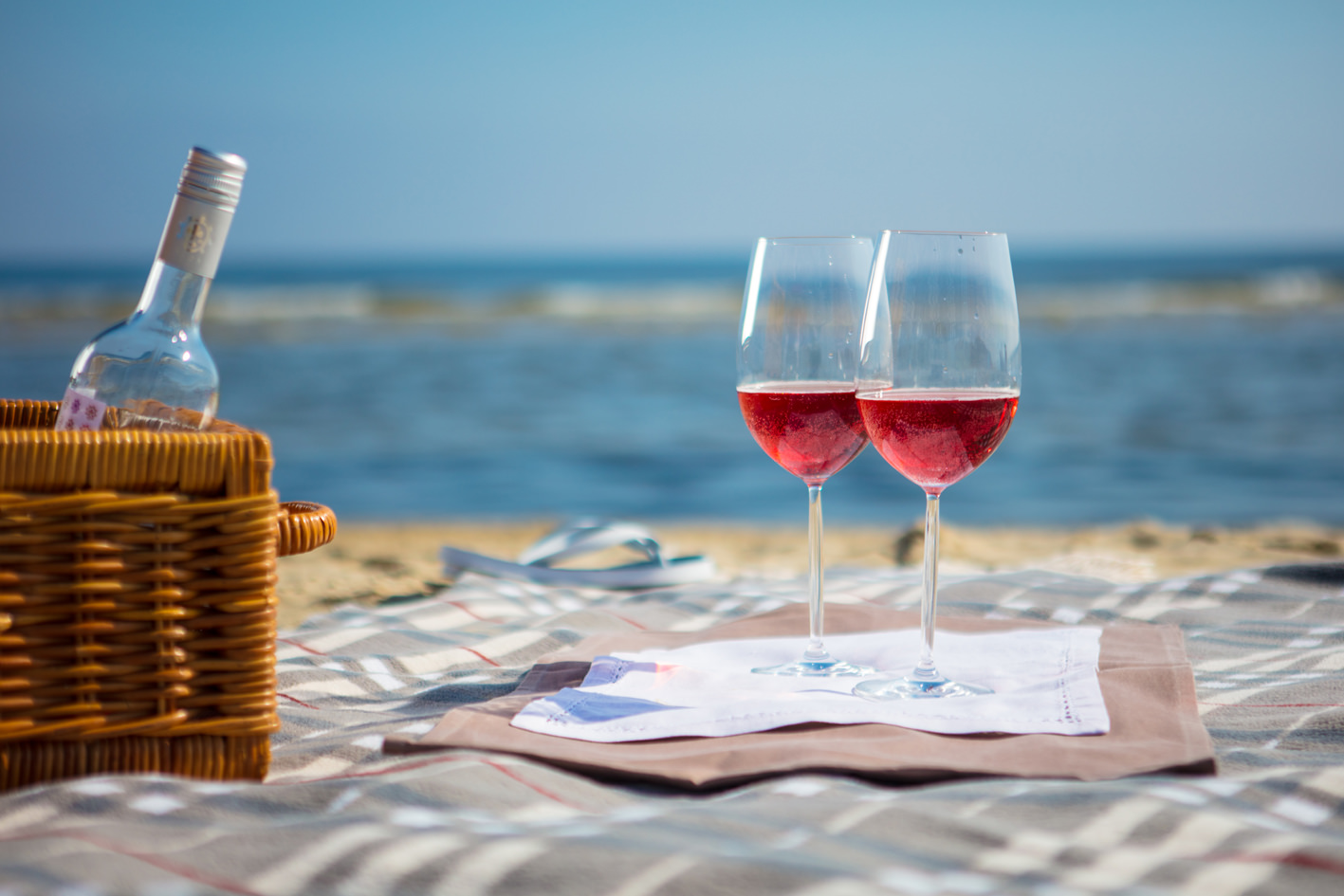 Zwei Weingläser, die auf einer Decke am Strand ausgebreitet liegt.